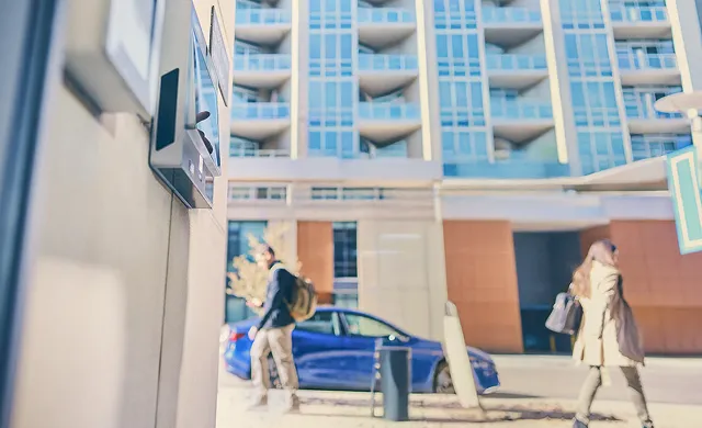 A man holds two packages and rings the doorbell of an apartment building.