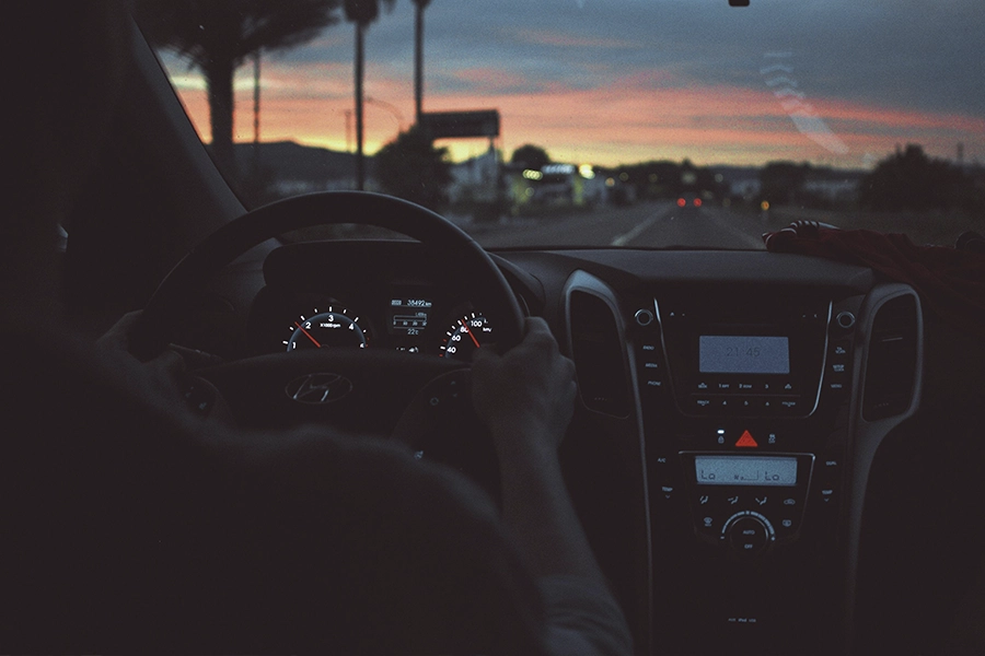 A photo shot from the backseat of the car with the dashboard and steering wheel silhoutted against a sunset outside the front window